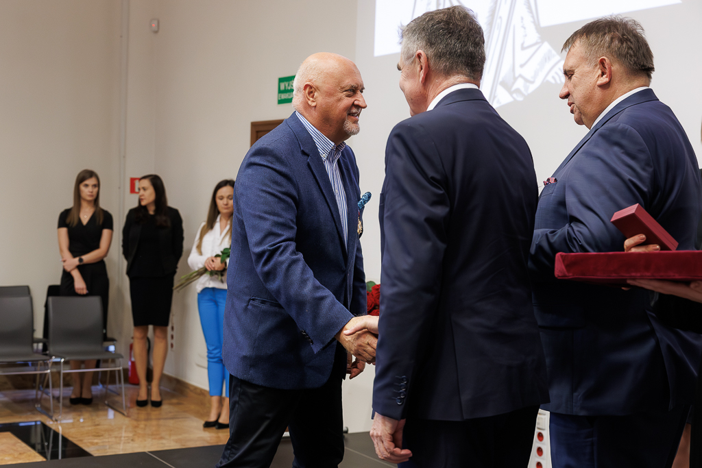 Prof. Tomasz Paszkowski uściskujący dłoń Lechowi Sprawce. Obok prof. Wojciech Załuska