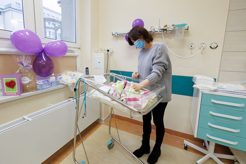 Jedna z mam ze swoim dzieckiem na sali w oddziale. W tle fioletowe balony.