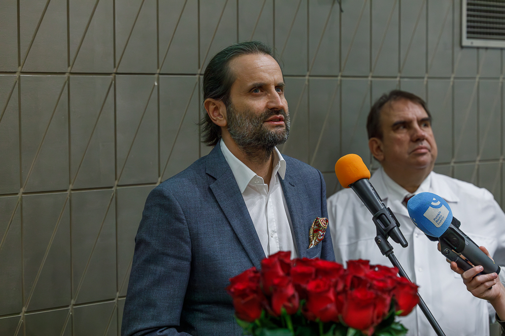 Wiceminister zdrowia Piotr Bromber i lekarz kierujący Kliniką Nefrologii SPSK Nr 4 w Lublinie prof. dr hab.n.med. Wojciech Załuska przed mikrofonami. Z przodu bukiet czerwonych róż.