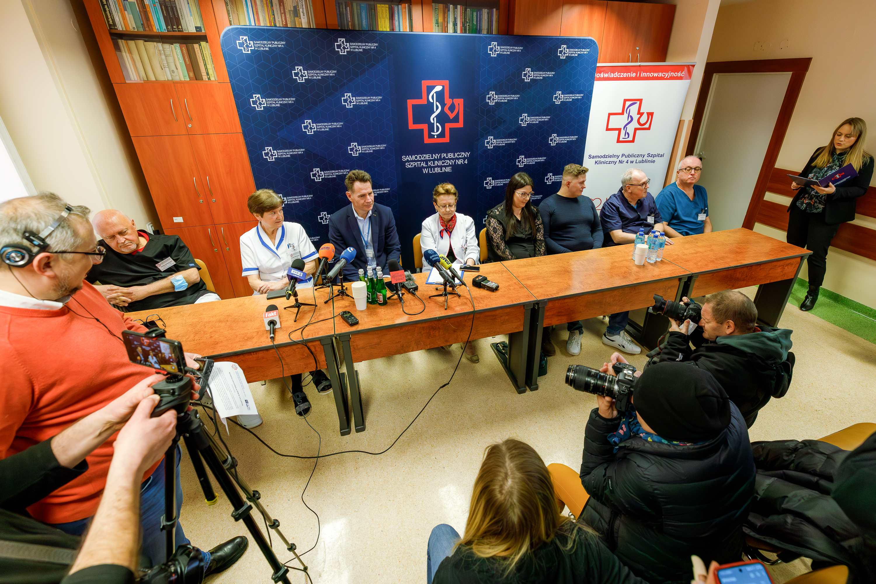 Stół, za którym siedzi 8 osób, z tyłu ścianka z napisami "Samodzielny Publiczny Szpital Kliniczny Nr 4 w Lublinie", z przodu dziennikarze