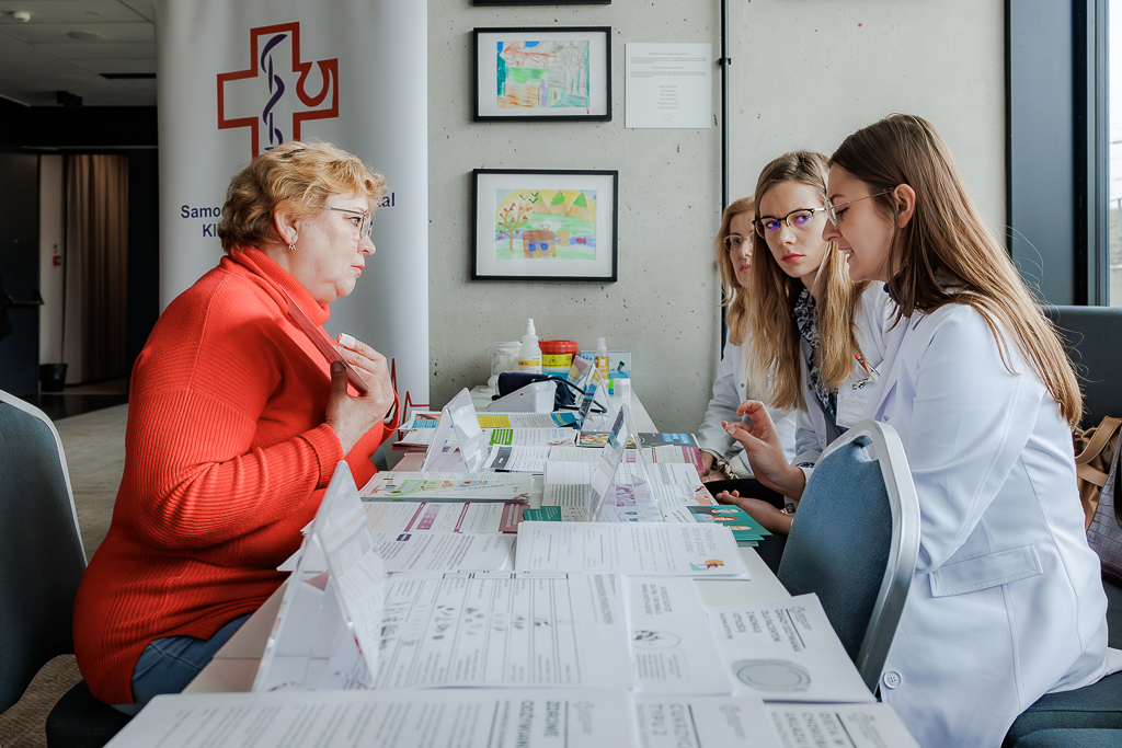 Seniorka siedząca przy stole słuchająca porad specjalistów SPSK Nr 4. 