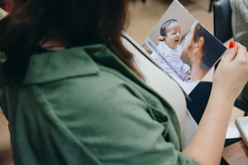 Uczestniczka spotkania ogląda jedną z kart motywacyjnych dla ojców. Na prostokątnej karcie jest ze zdjęciem ojca i noworodka jest napis: Obecność od pierwszych dni życia.