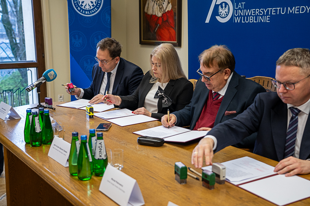 Moment podpisania umowy. Przy stole siedzą sygnatariusze - dyrektor USK Nr 4, dyrektor szpitala w Świdniku, rektor Uniwersytetu Medycznego w Lublinie i członek zarządu powiatu świdnickiego. Są pochyleni nad podpisywanym dokumentem.