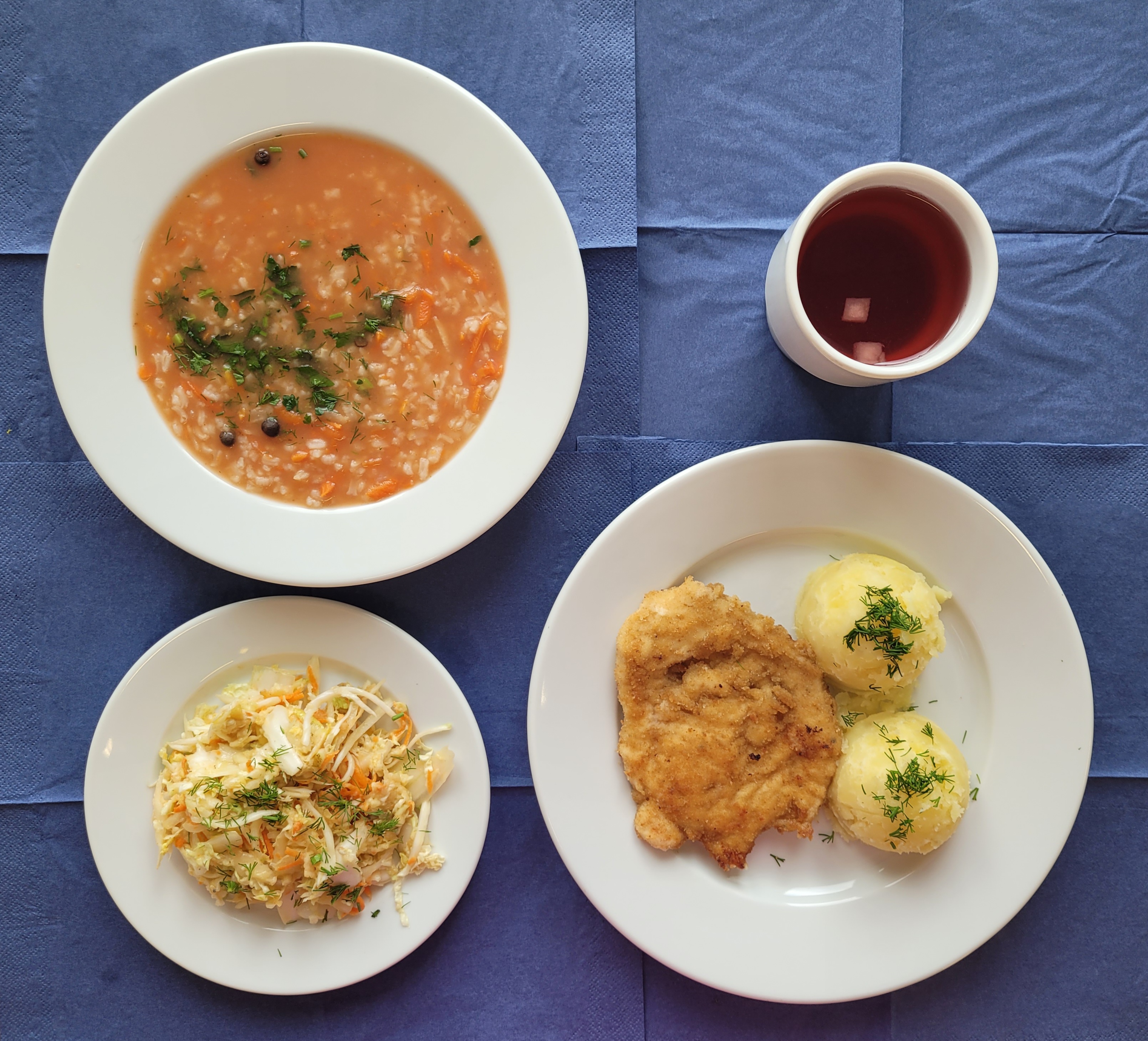 na talerzach zupa pomidorowa z ryżem, kotlet drobiowy panierowany smażony, ziemniaki gotowane, surówka z kapusty pekińskiej, marchewki i sosu vinegret, w kubku kompot 