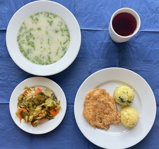 na talerzach zupa koperkowa z makaronem, kotlet drobiowy smażony, ziemniaki, surówka z ogórka kiszonego, marchewki w kubku kompot 