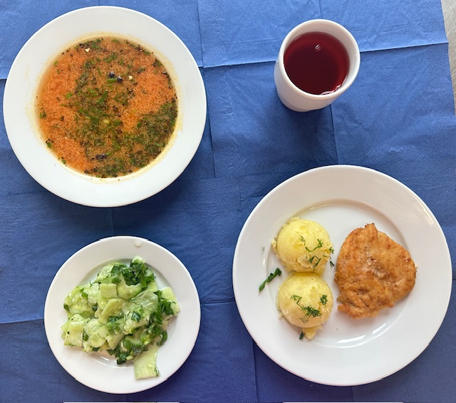 na talerzach zupa pomidorowa z makaronem, kotlet drobiowy smażony, ziemniaki, mizeria, w kubku kompot 