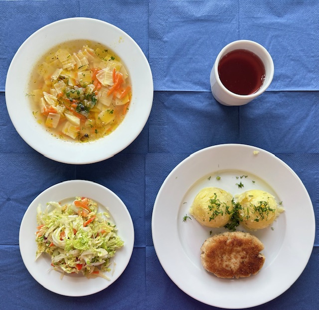 na talerzach zupa zacierka, kotlet rybny smażony, ziemniaki, surówka z kapusty pekińskiej i papryki, w kubku kompot 