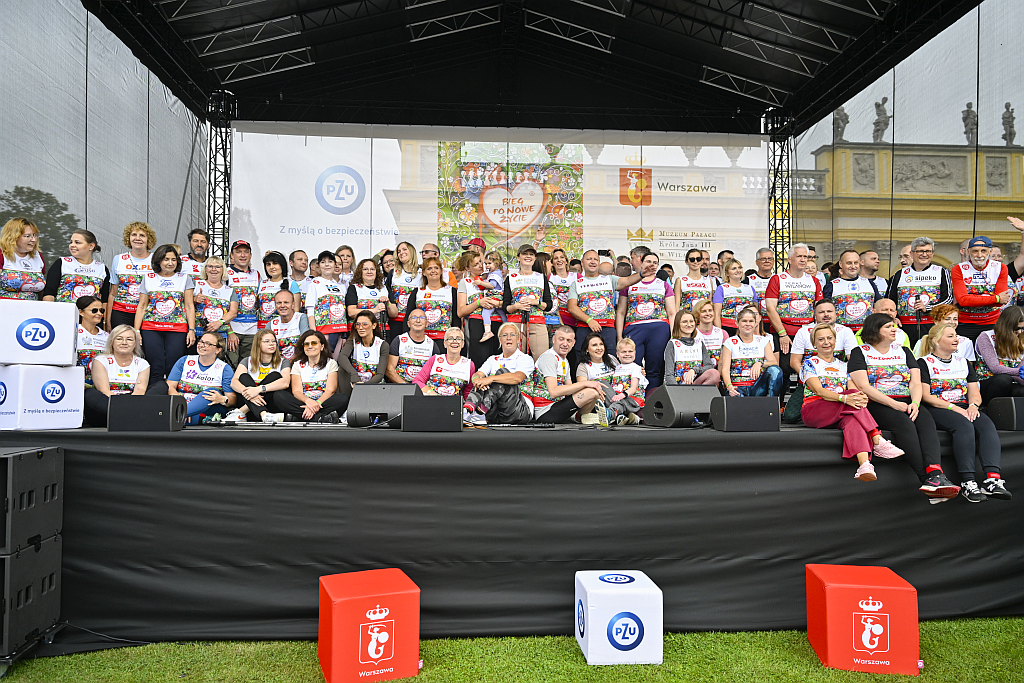 Zdjęcie grupowe osób po transplantacji, które uczestniczyły w tegorocznym Biegu. Uczestnicy wydarzenia stoją i siedzą obok siebie. Znajdują się na scenie.