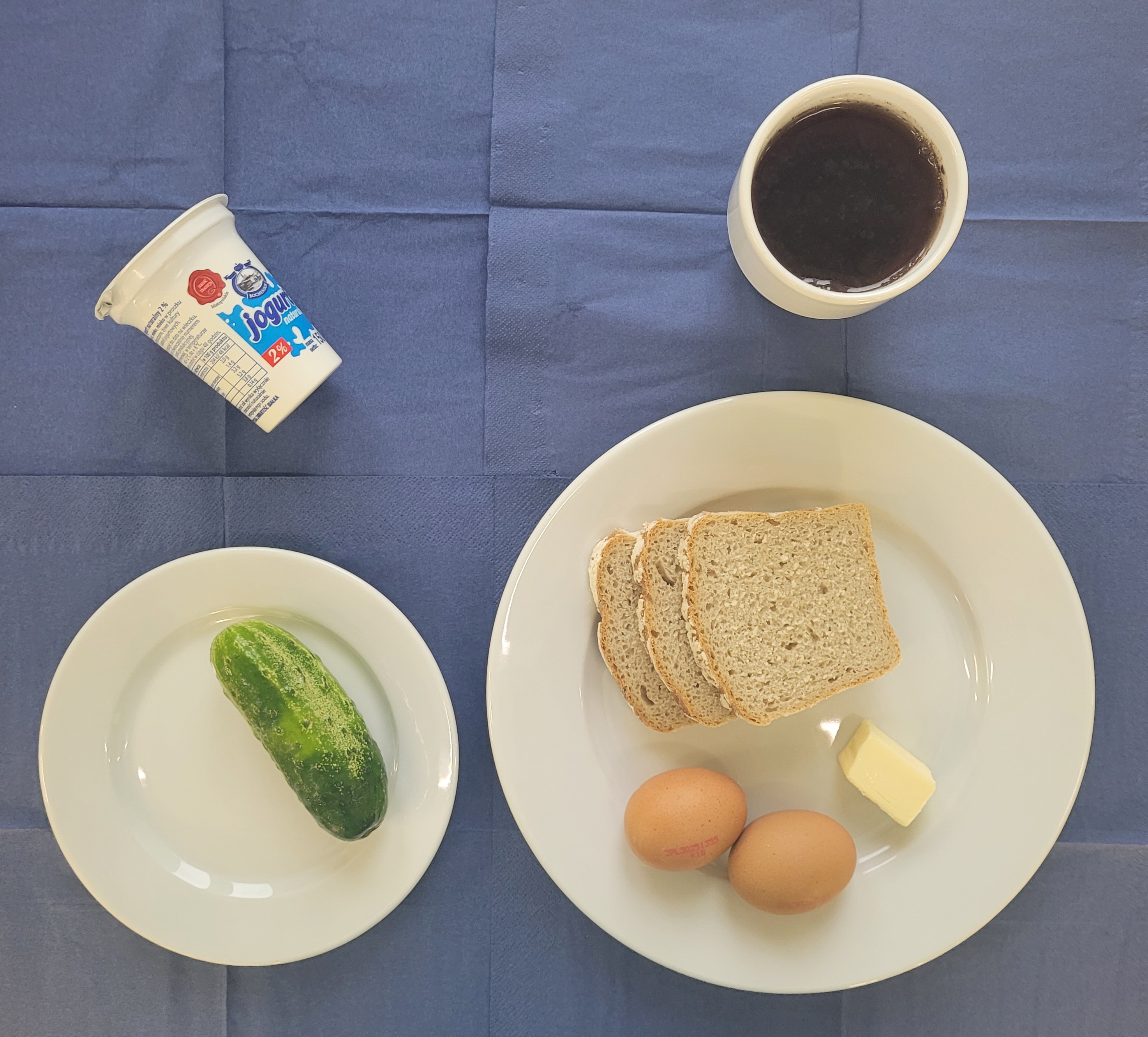 Na talerzach: jaja, ogórek świeży , masło, chleb razowy, jogurt naturalny, w kubku herbata z cytryną bez cukru