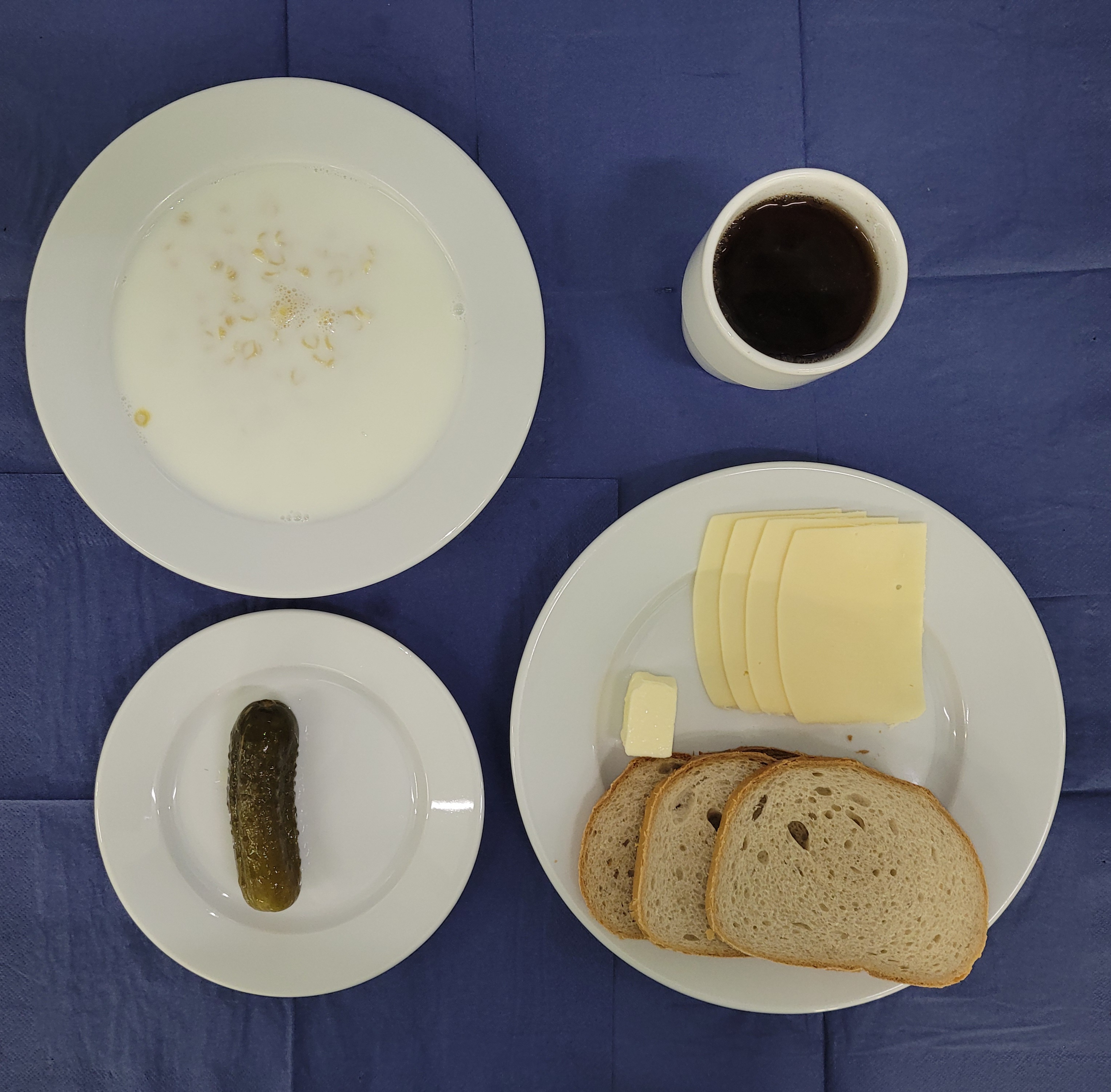 na talerzach makaron na mleku, chleb pszenny, chleb zwykły, masło, ser żółty, ogórek kiszony, w kubku herbata z cytryną