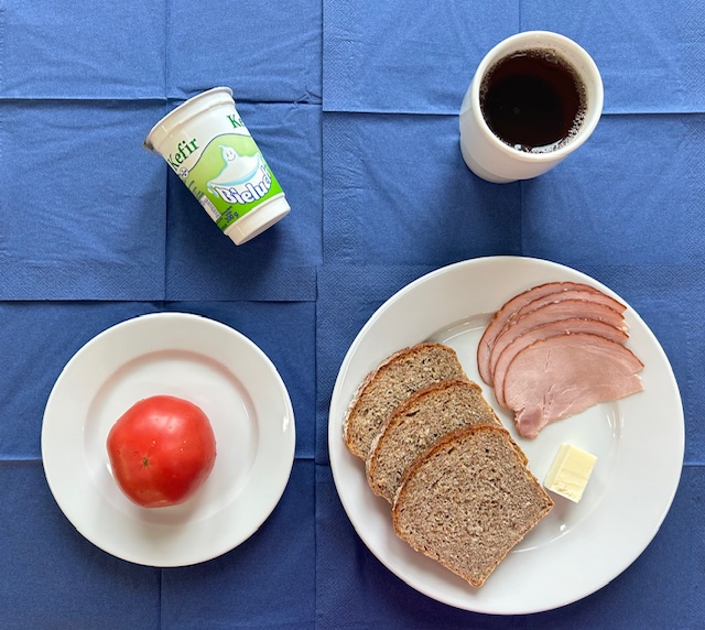 na talerzach chleb razowy, masło, szynka drobiowa, pomidor, kefir, w kubku herbata z cytryną