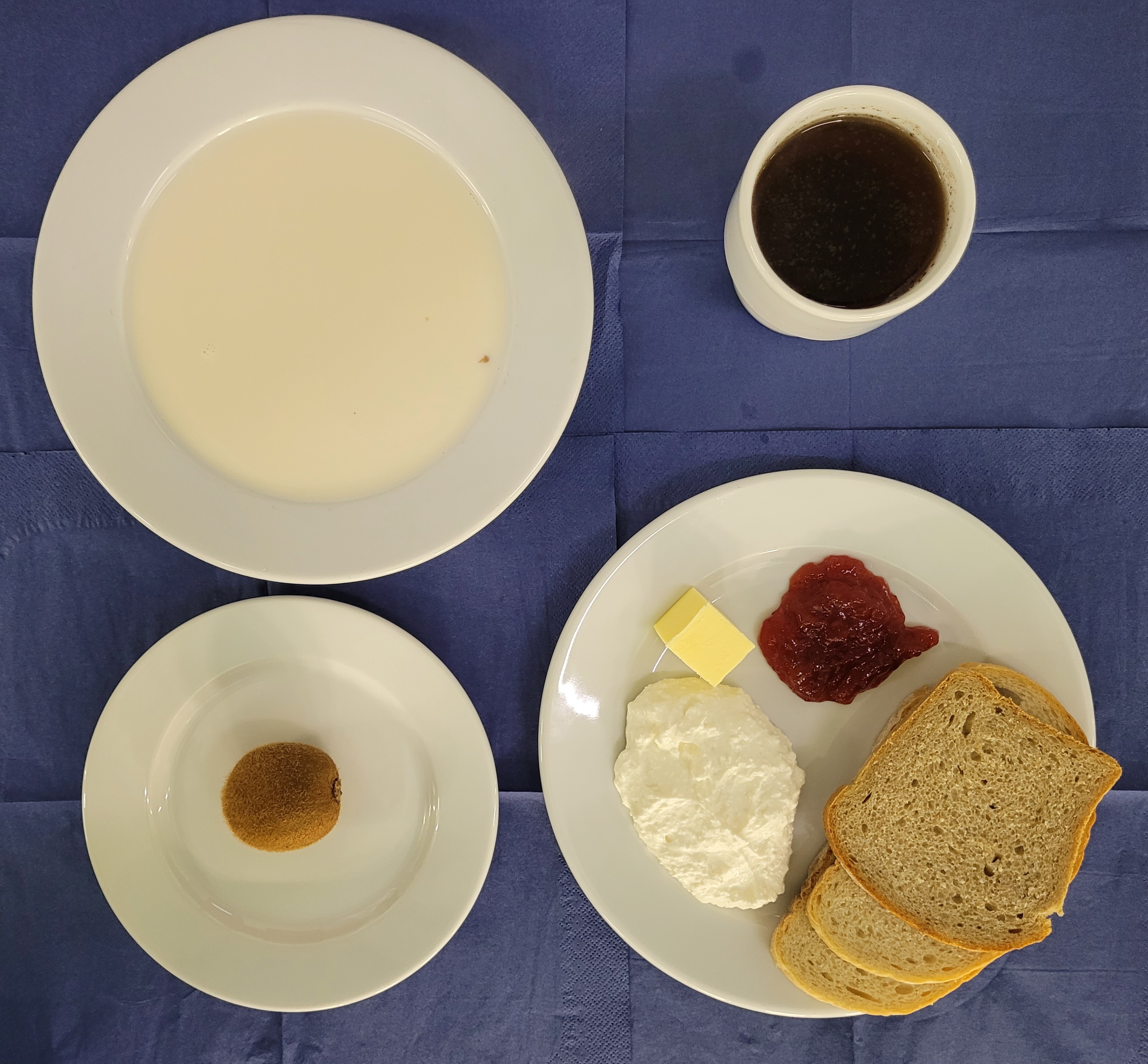 na talerzach kasza gryczana na mleku, chleb pszenny, chleb sitkowy, masło, ser biały, dżem, kiwi, w kubku herbata z cytryną