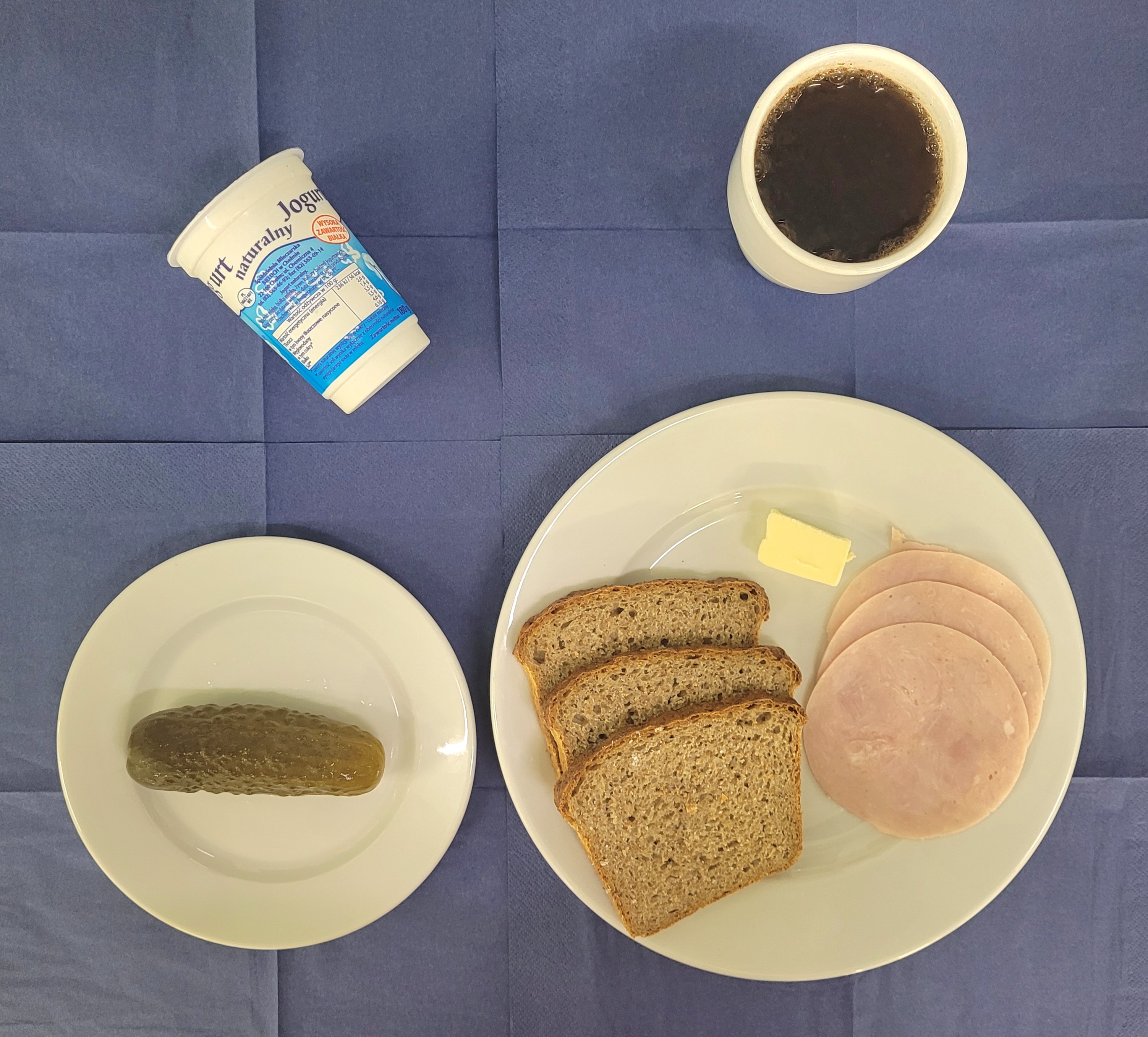 na talerzach chleb razowy, masło, szynkowa, ogórek kiszony, jogurt naturalny, w kubku herbata z cytryną