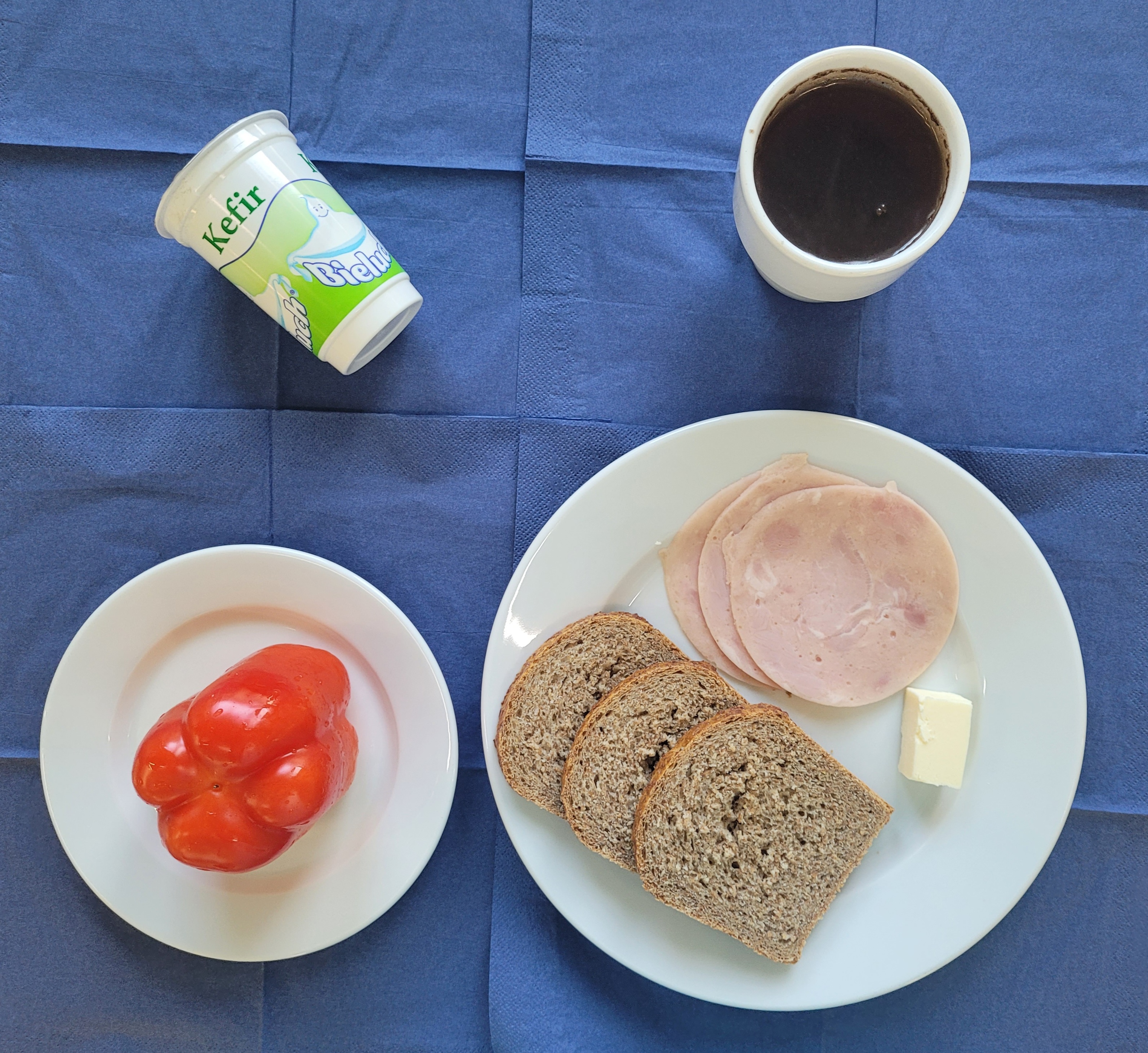 na talerzach chleb razowy, masło, wędlina szynkowa, papryka, kefir, w kubku herbata z cytryną bez cukru