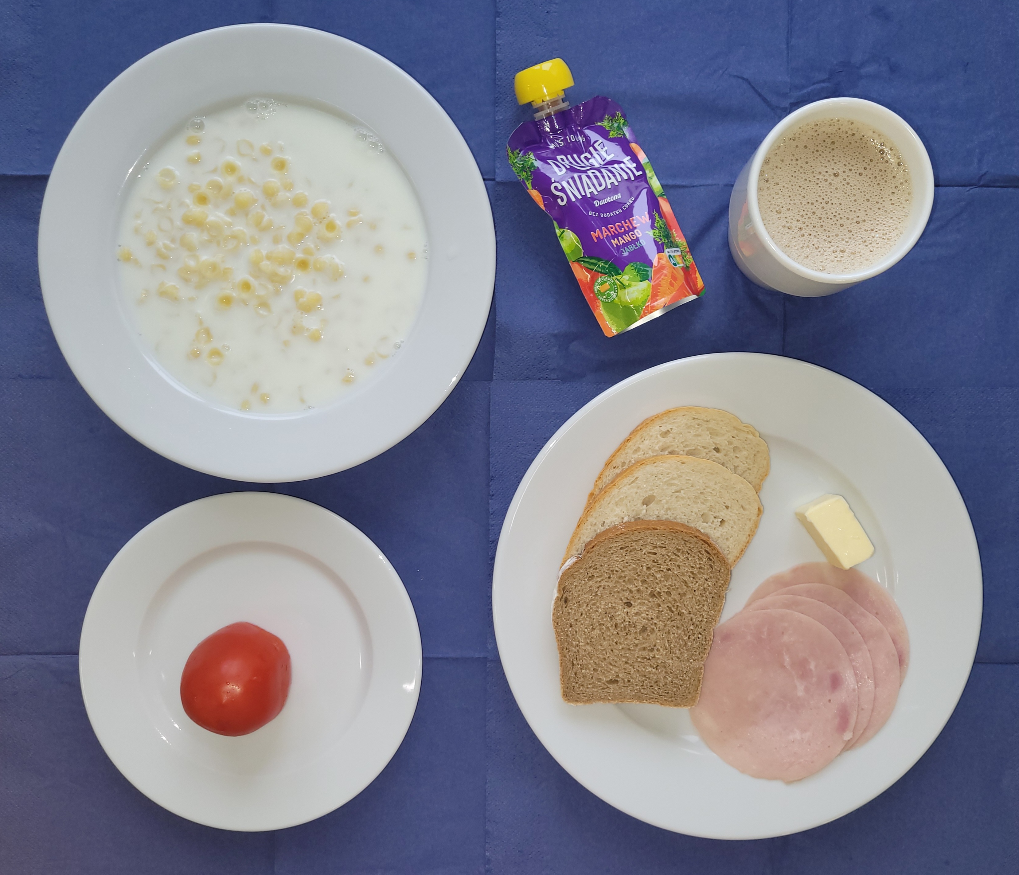 na talerzach makaron na mleku, chleb pszenny, chleb sitkowy, masło, pomidor, kawa zbozowa, mus warzywno-owocowy