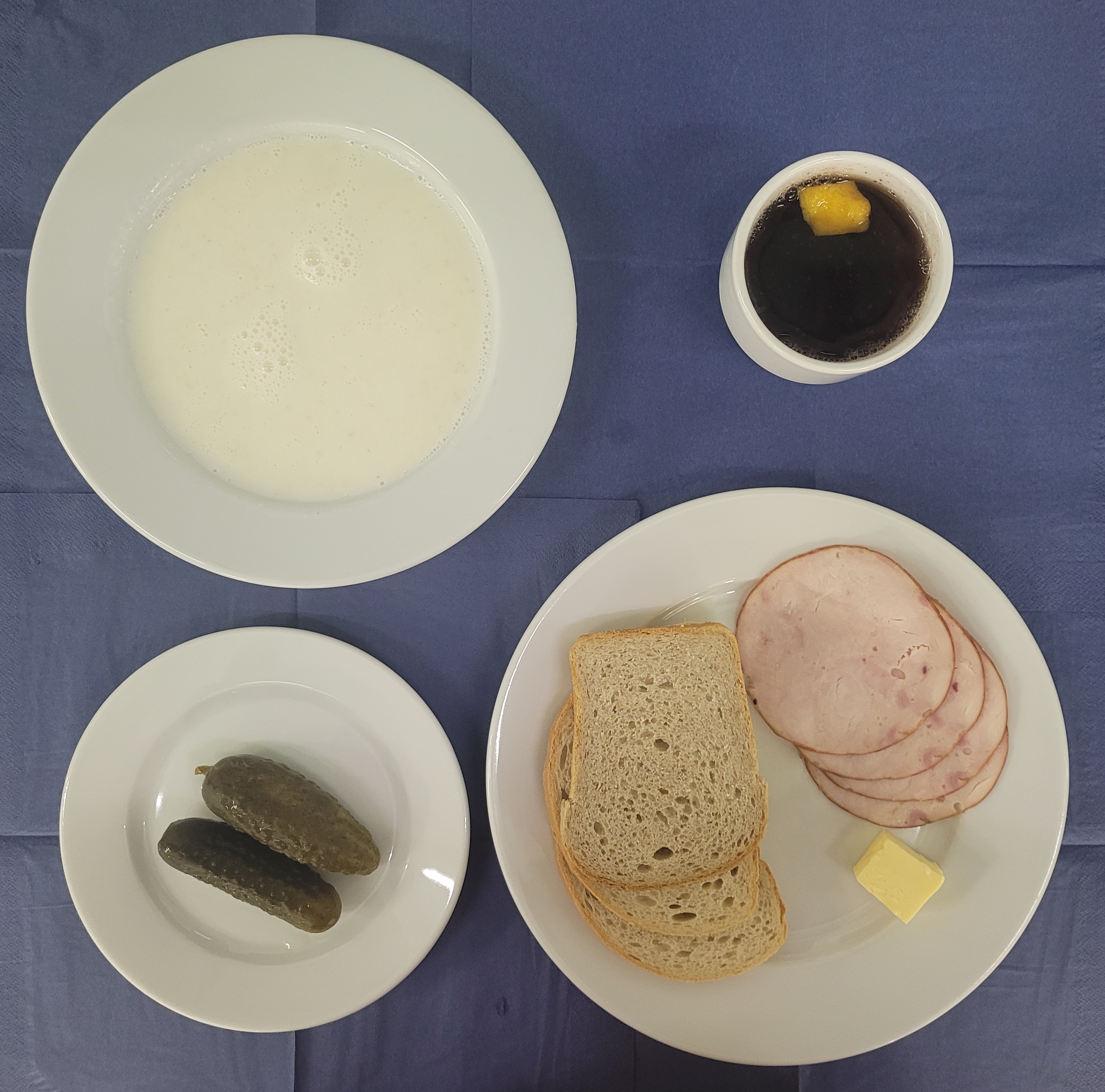 na talerzach płatki jaglane na mleku, chleb pszenny, chleb sitkowy, baleron z indyka, masło, ogórek kiszony, herbata z cytryną w kubku 