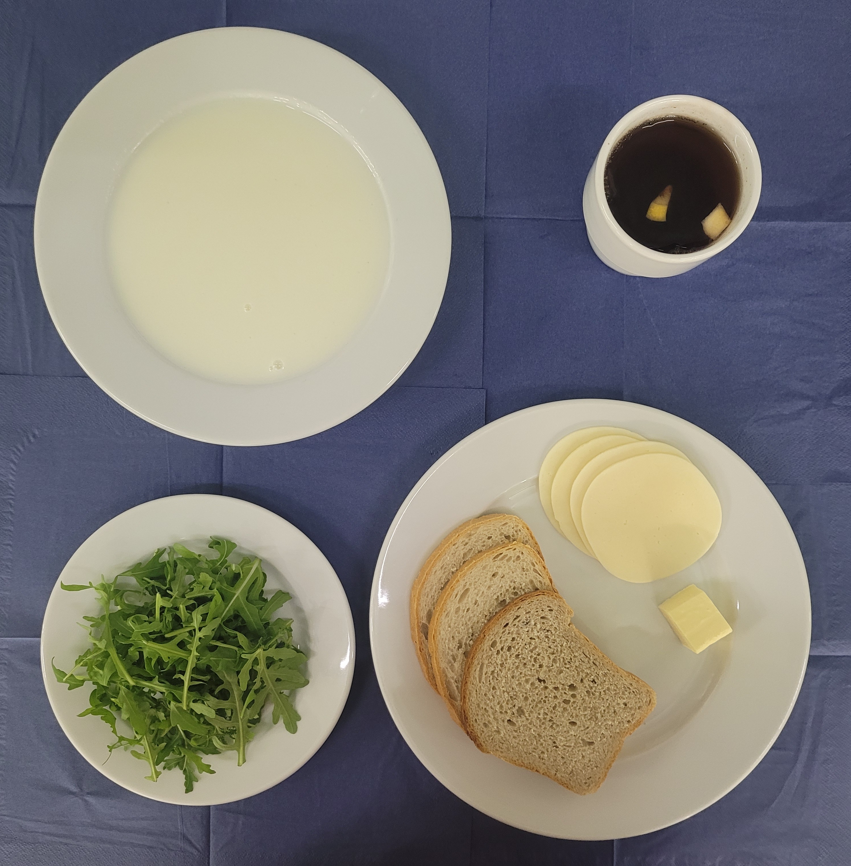 na talerzach kasza manna na mleku, chleb pszenny, chleb sitkowy, masło, ser żółty, rukola, w kubku herbata z cytryną 