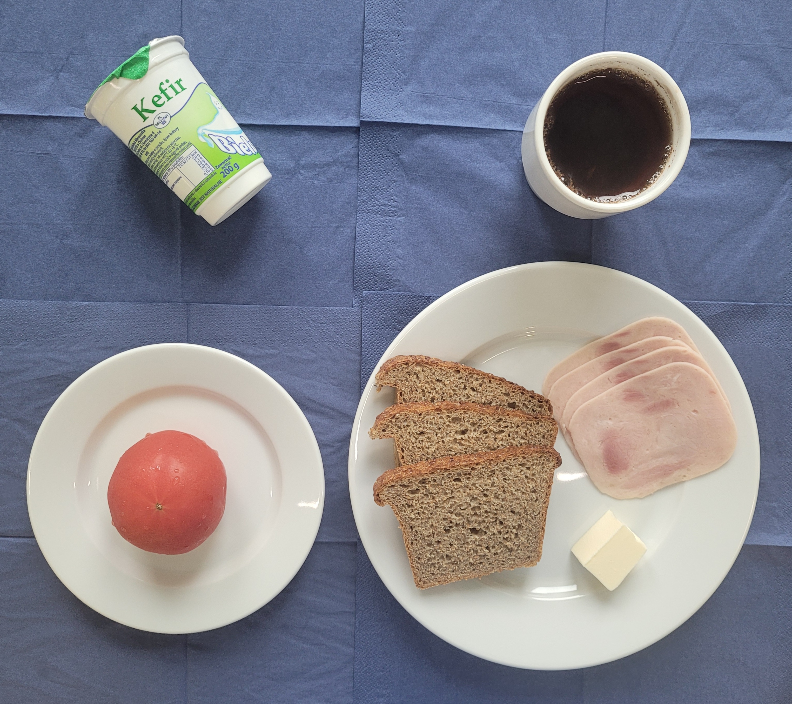 na talerzach chleb razowy, masło, szynka lubelska, pomidor, kefir, w kubku herbata z cytryną 
