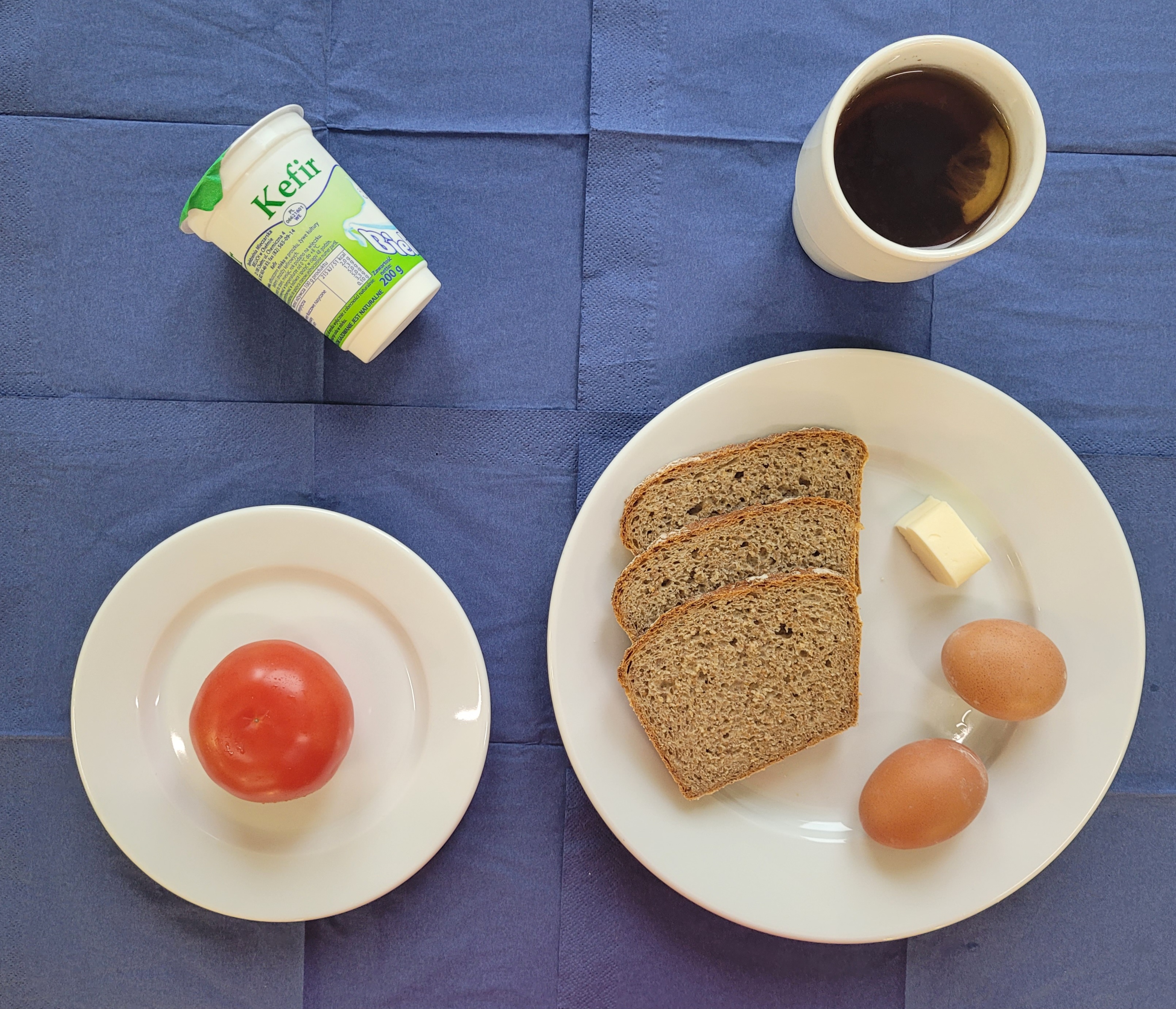 na talerzach chleb razowy, masło, jajko gotowane 2 sztuki, pomidor, kefir, w kubku herbata z cytryną