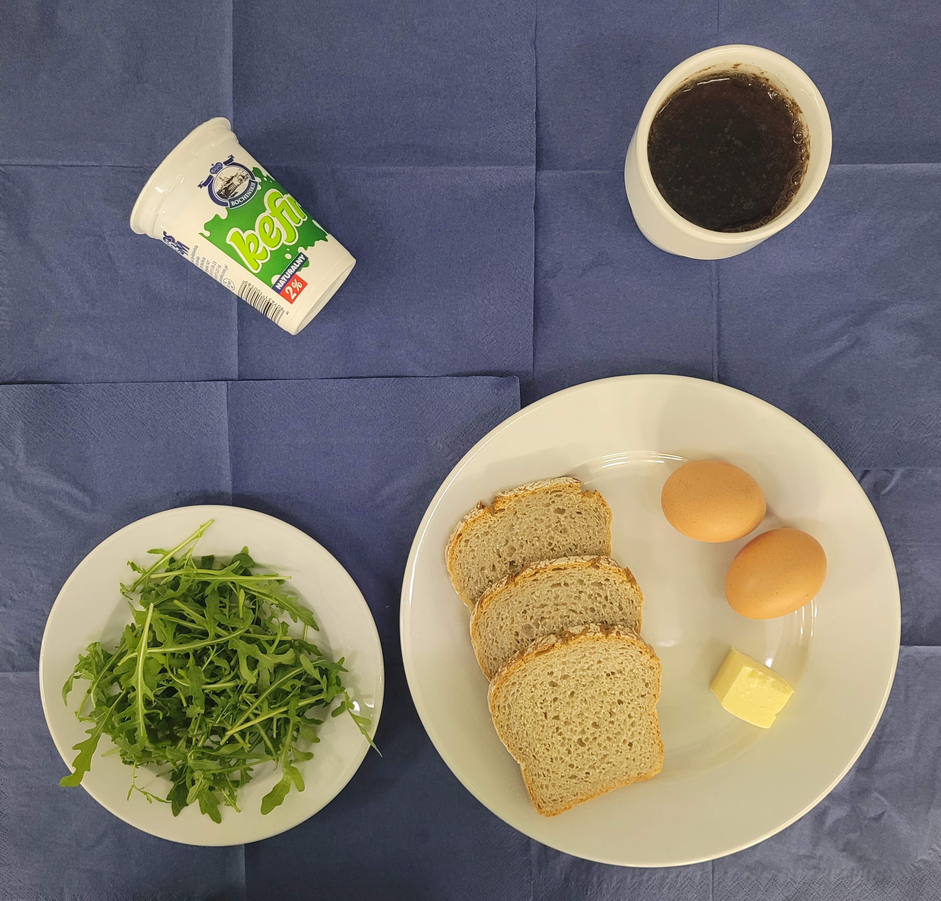 na talerzach chleb razowy, masło, jajko gotowane 2 sztuki, rukola, kefir , herbata z cytryną