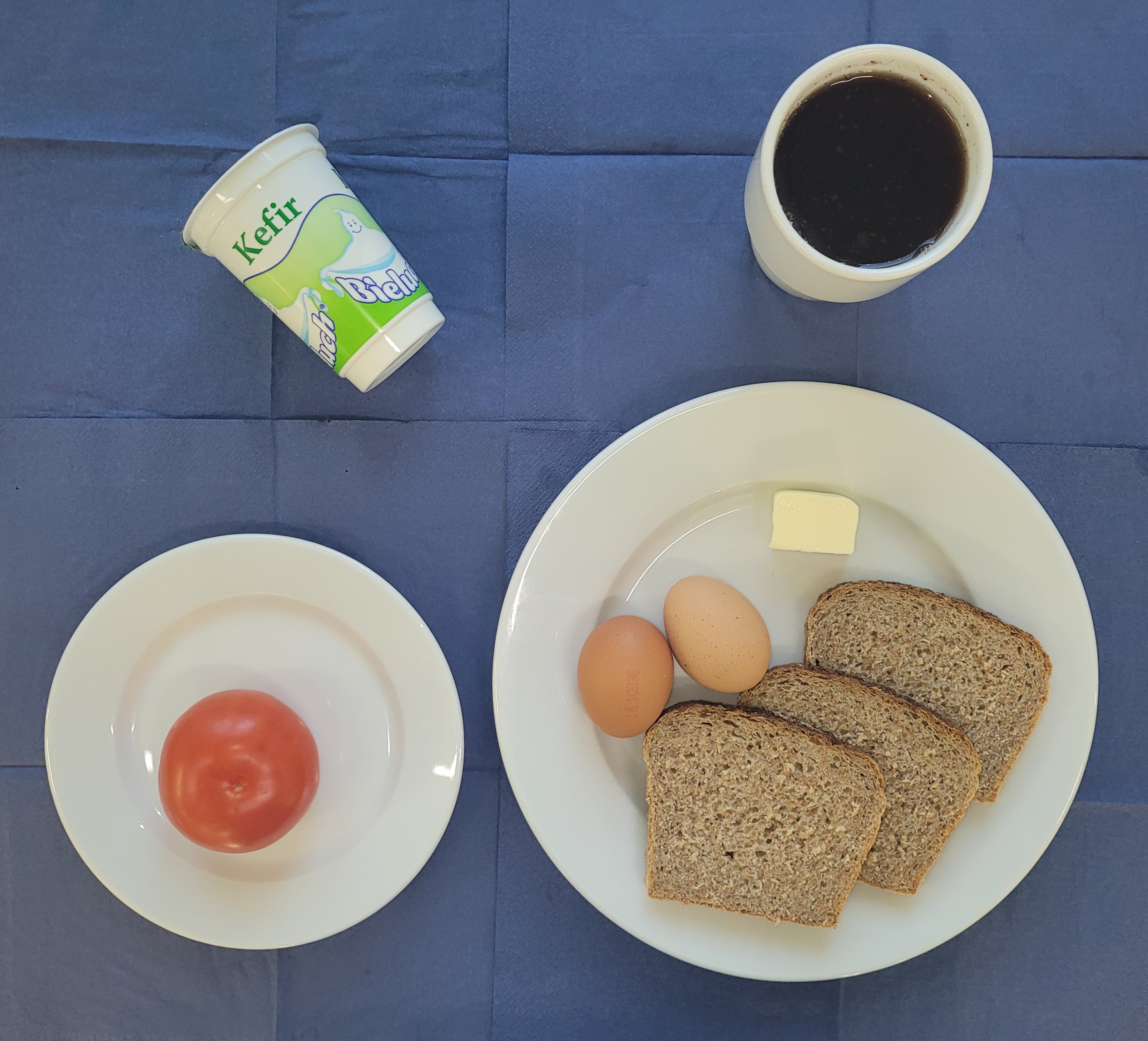 na talerzach chleb razowy, jajko gotowane 2 sztuki, masło, pomidor, kefir w kubku herbata z cytryną