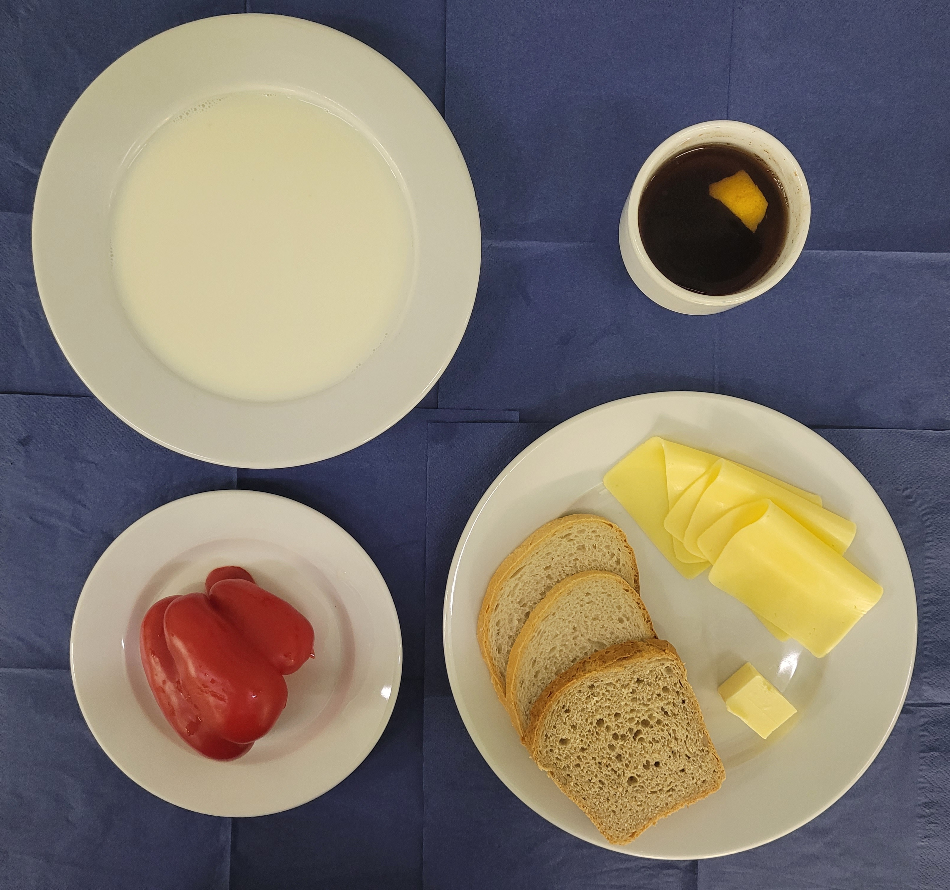 na talerzach kasza jaglana na mleku, chleb sitkowy, chleb zwykły, ser żółty, masło, papryka, w kubku herbata z cytryną słodka 