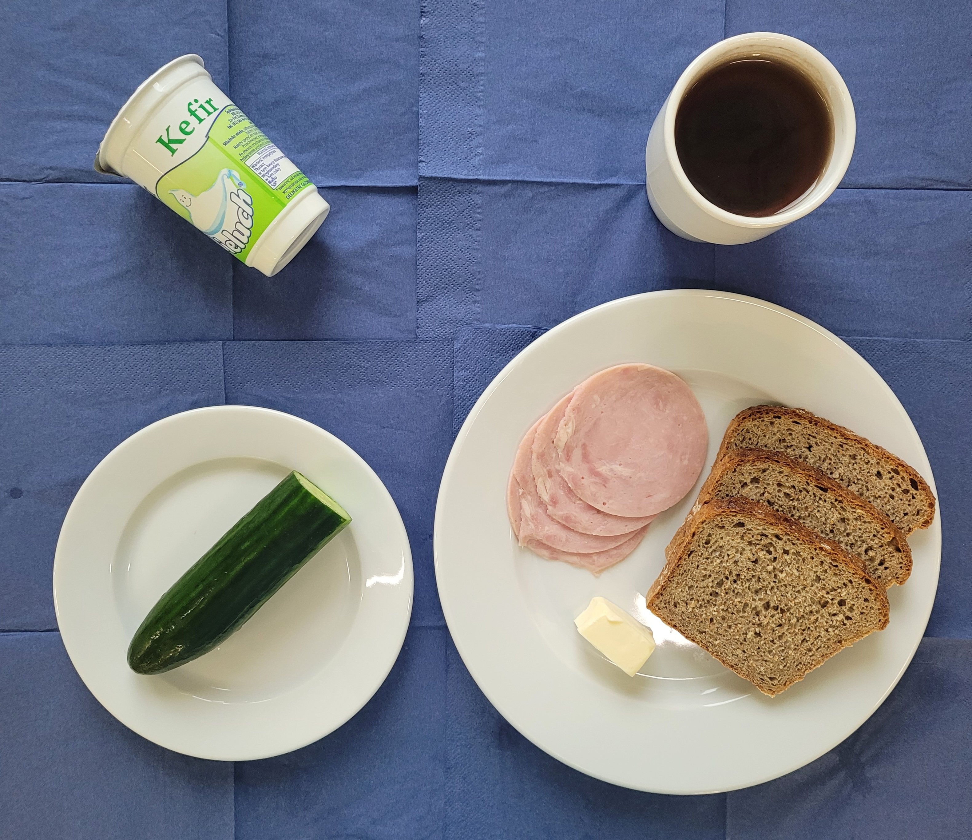 na talerzach chleb razowy, masło, polędwicowa, ogórek świeży, kefir, herbata z cytryną bez cukru