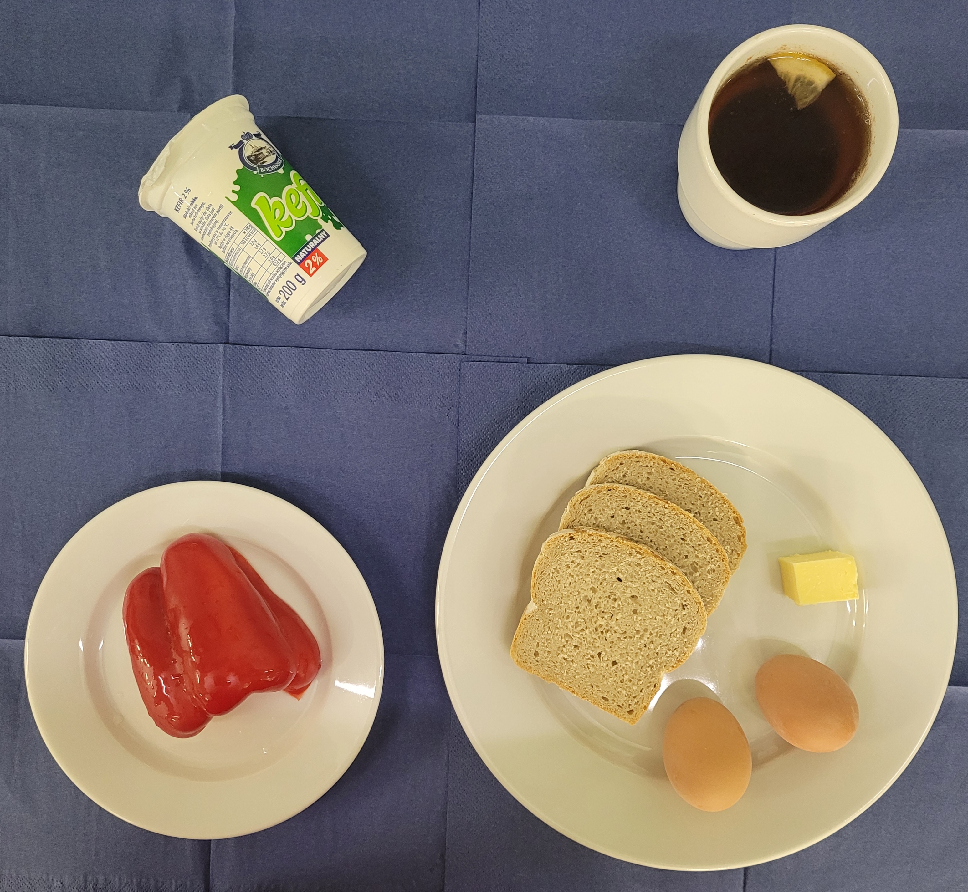 na talerzach chleb razowy, jajko gotowane 2 sztuki, masło, papryka, kefir, w kubku herbata z cytryną