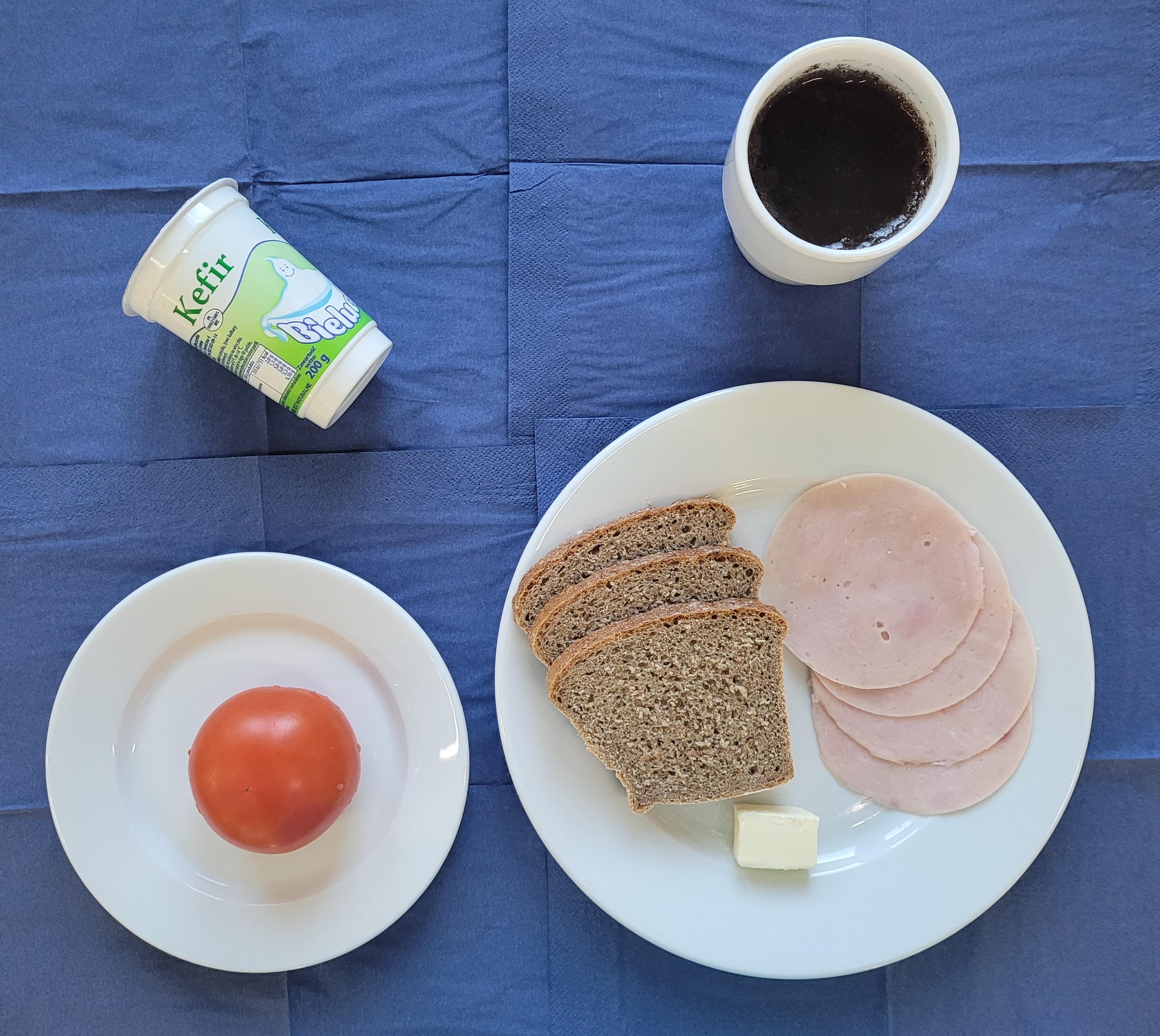 na talerzach chleb razowy, masło, wędlina szynkowa, pomidor, kefir, w kubku herbata z cytryną 