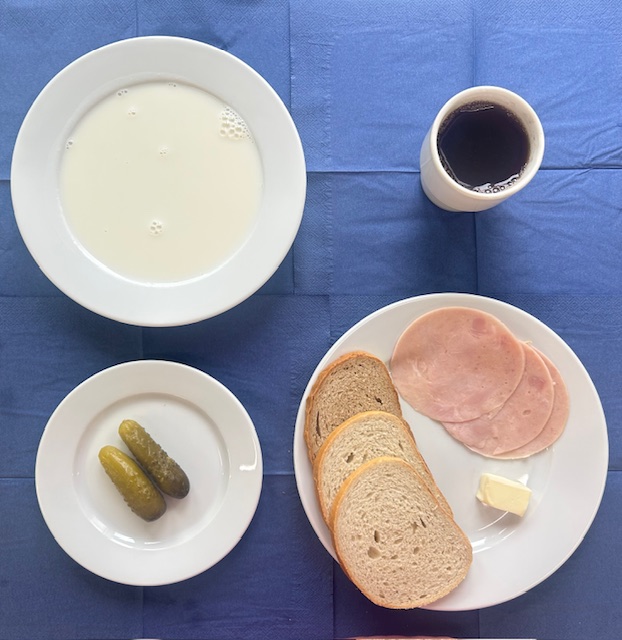na talerzach kasza jęczmienna na mleku, chleb pszenny, chleb sitkowy, masło, polędwicowa, ogórek kiszony, w kubku herbata z cytryną i cukrem 