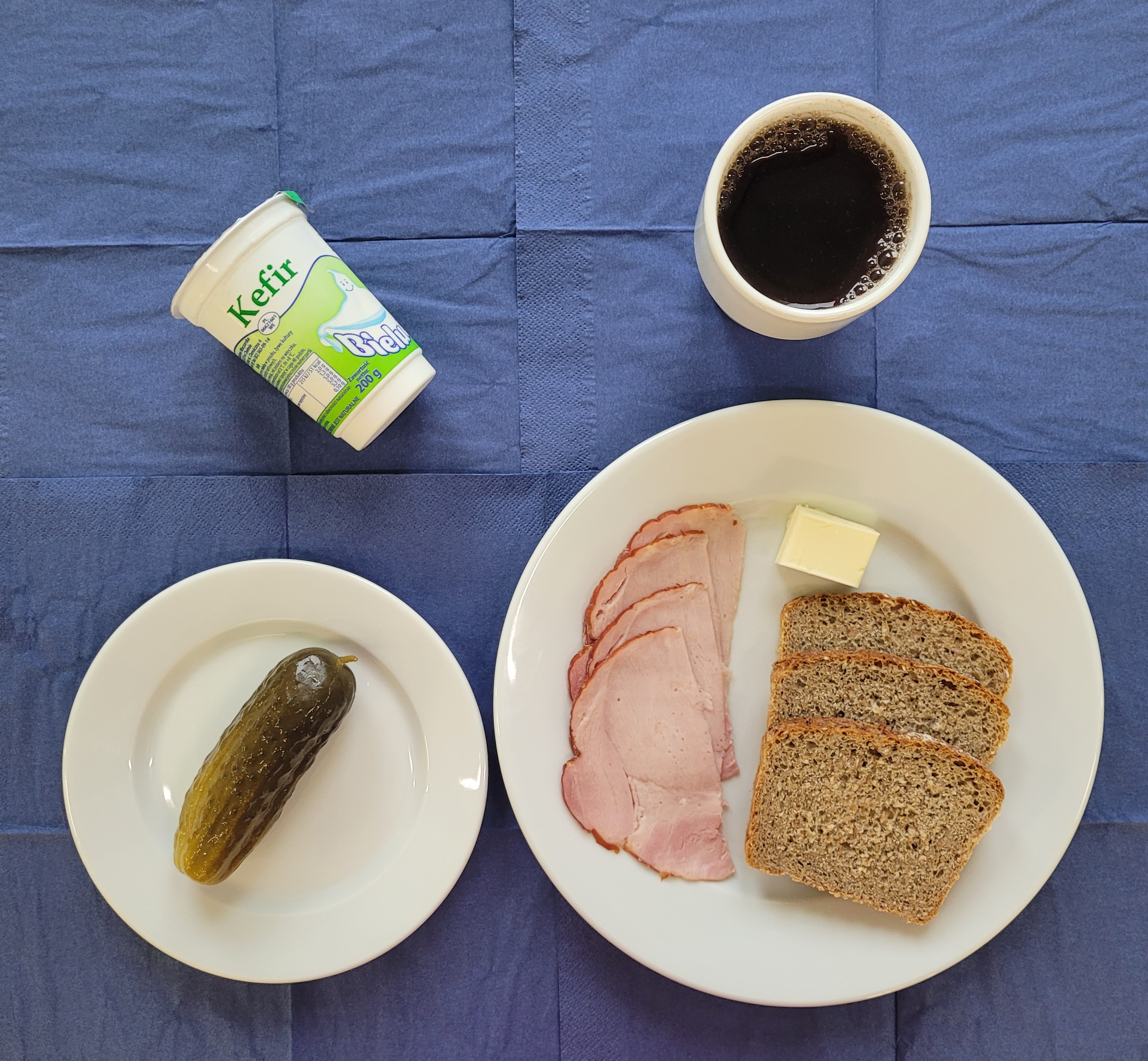 na talerzach chleb razowy, maso, szynka gotowana, ogórek kiszony, kefir, w kubku herbata z cytryną 