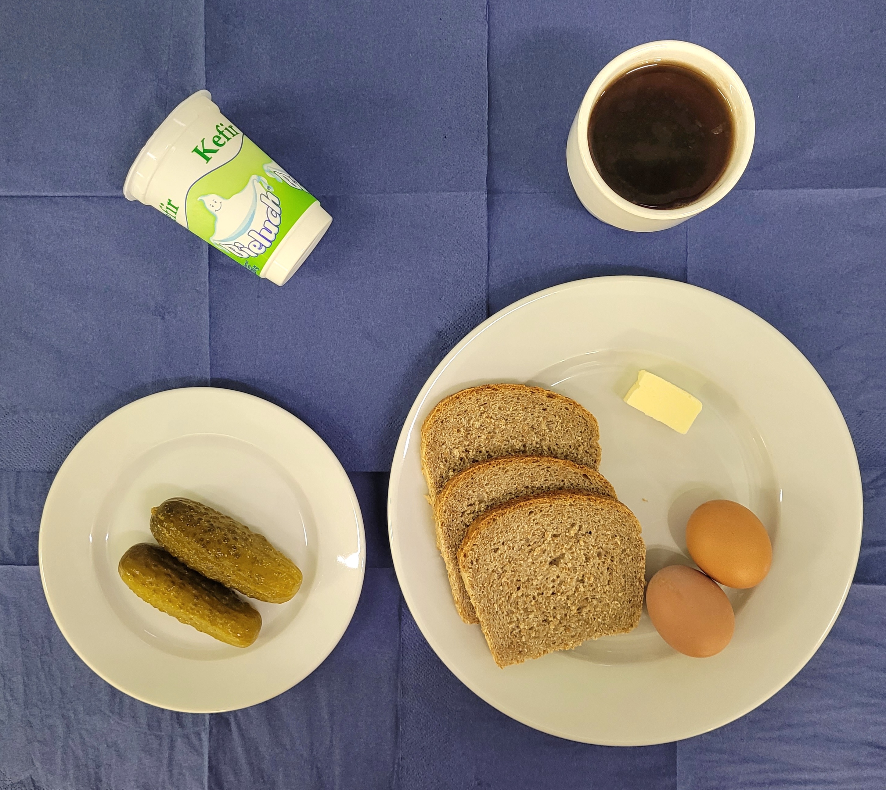 na talerzach chleb razowy, masło, ogórek kiszony, jajko gotowane 2 sztuki, kefir, w kubku herbata gorzka