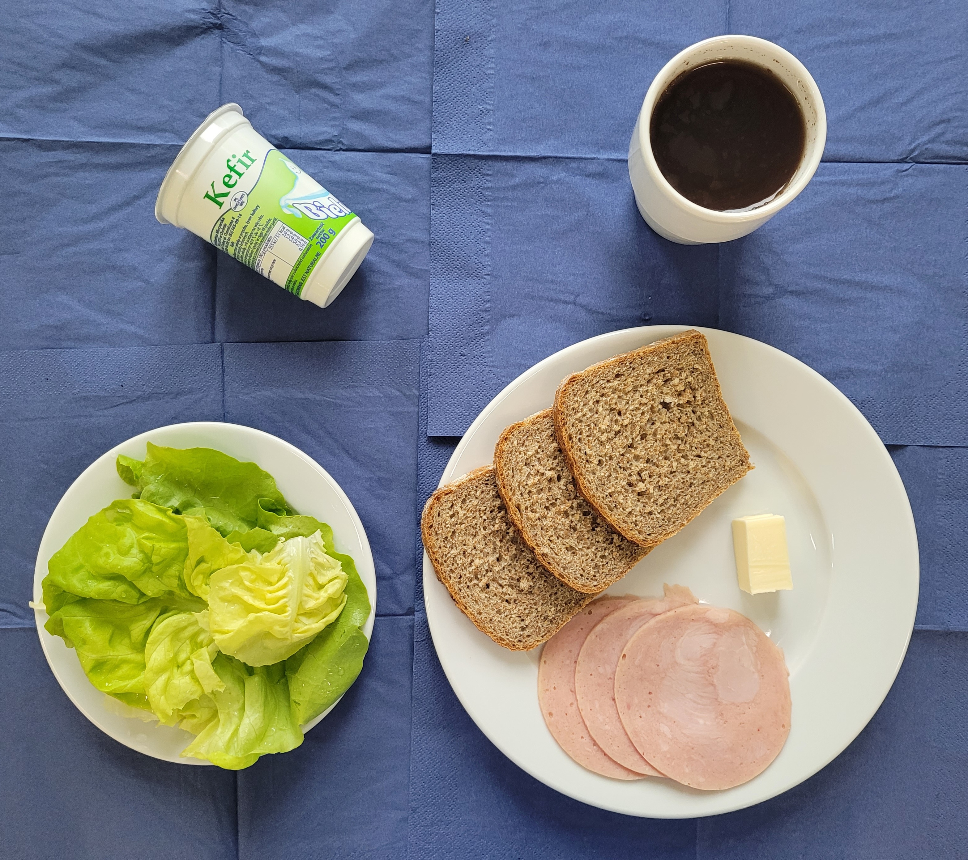 na talerzach chleb razowy, masło, szynkowa, sałata, kefir, w kubku herbata z cytryną 