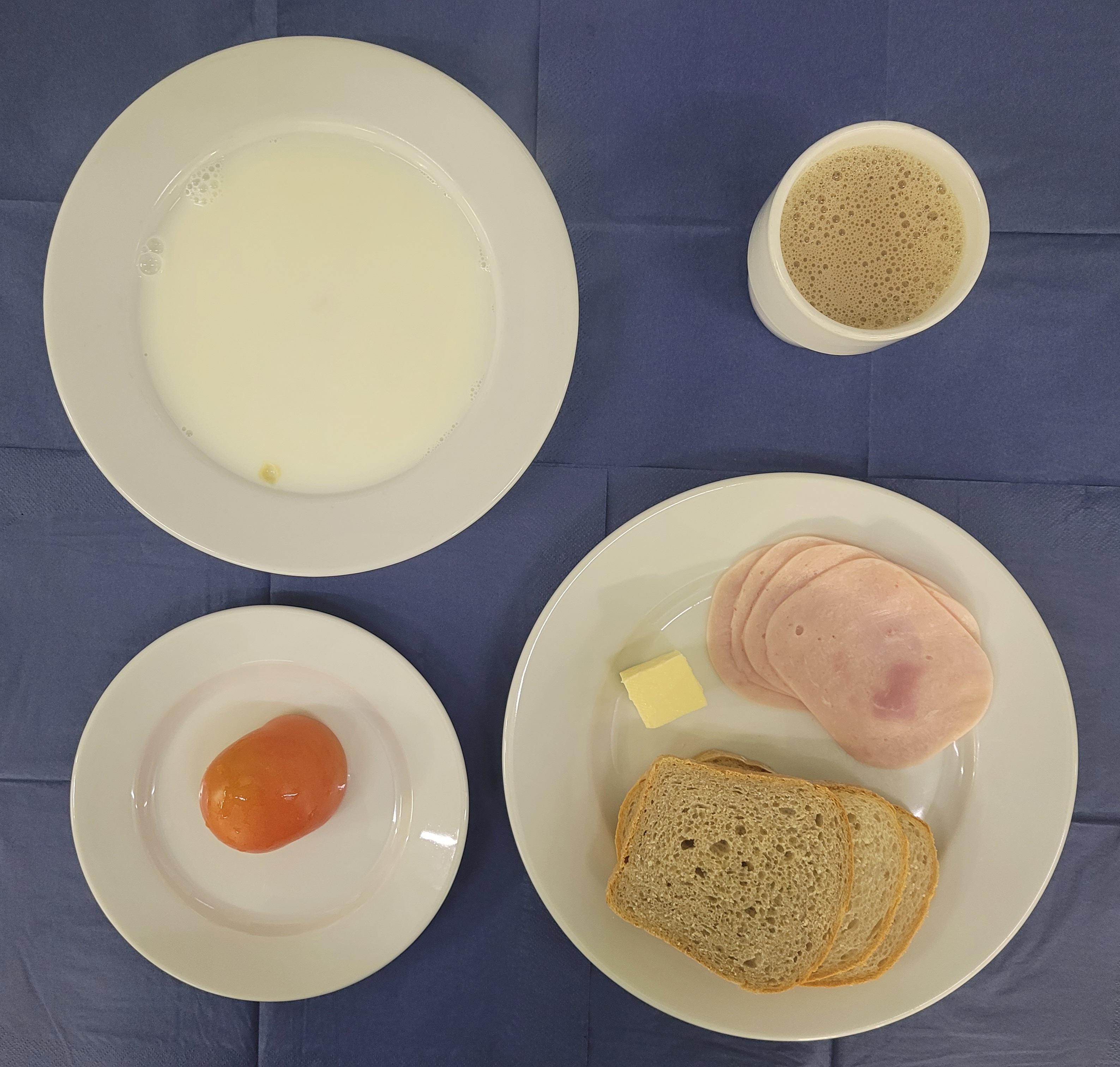 na talerzach makaron na mleku, szynka lubelska, chleb sitkowy, chleb pszenny, masło, pomidor, w kubku kawa zbożowa na mleku