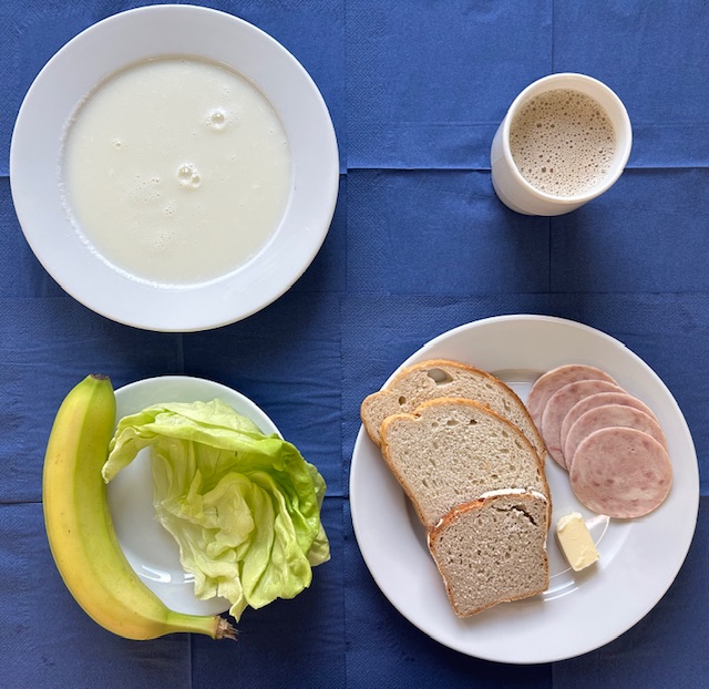 na talerzach kasza manna na mleku, baleron z indyka, chleb pszenny, chleb sitkowy, masło, sałata, banan, w kubku kawa zbożowa na mleku