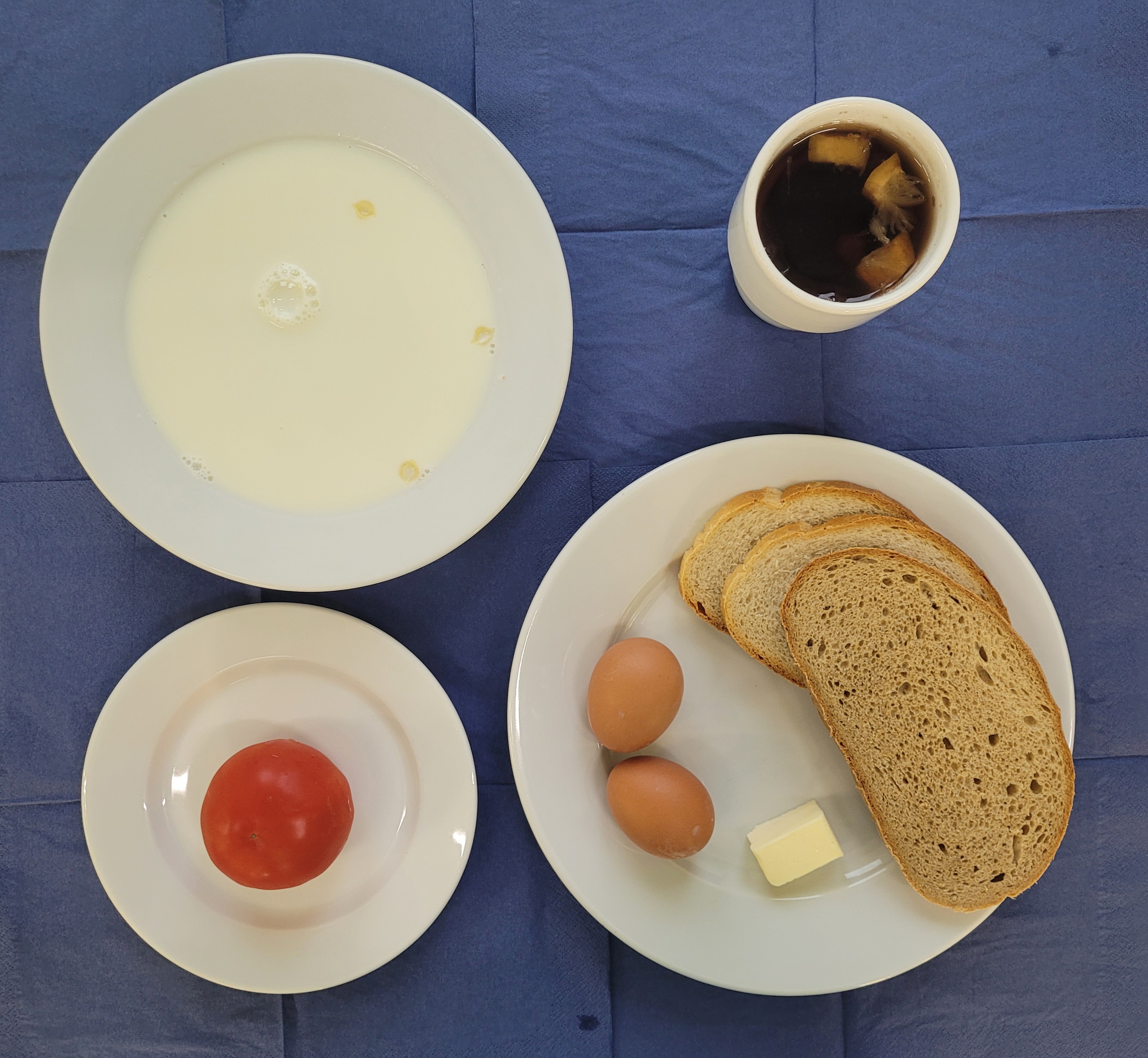 na talerzach makaron na mleku, chleb pszenny, chleb sitkowy, masło, jajko gotowane 2 sztuki, pomidor, w kubku herbata z cytryną